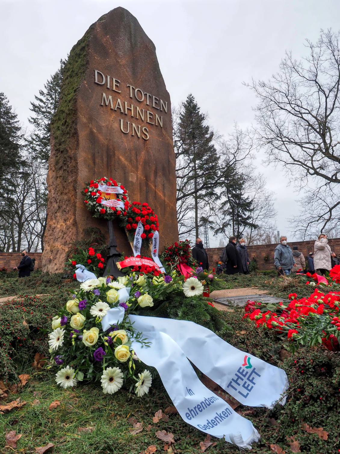 Gedenkstein mit der Inschrift "Die Toten mahnen uns", davor liegen Gedenkkränze und Blumengestecke