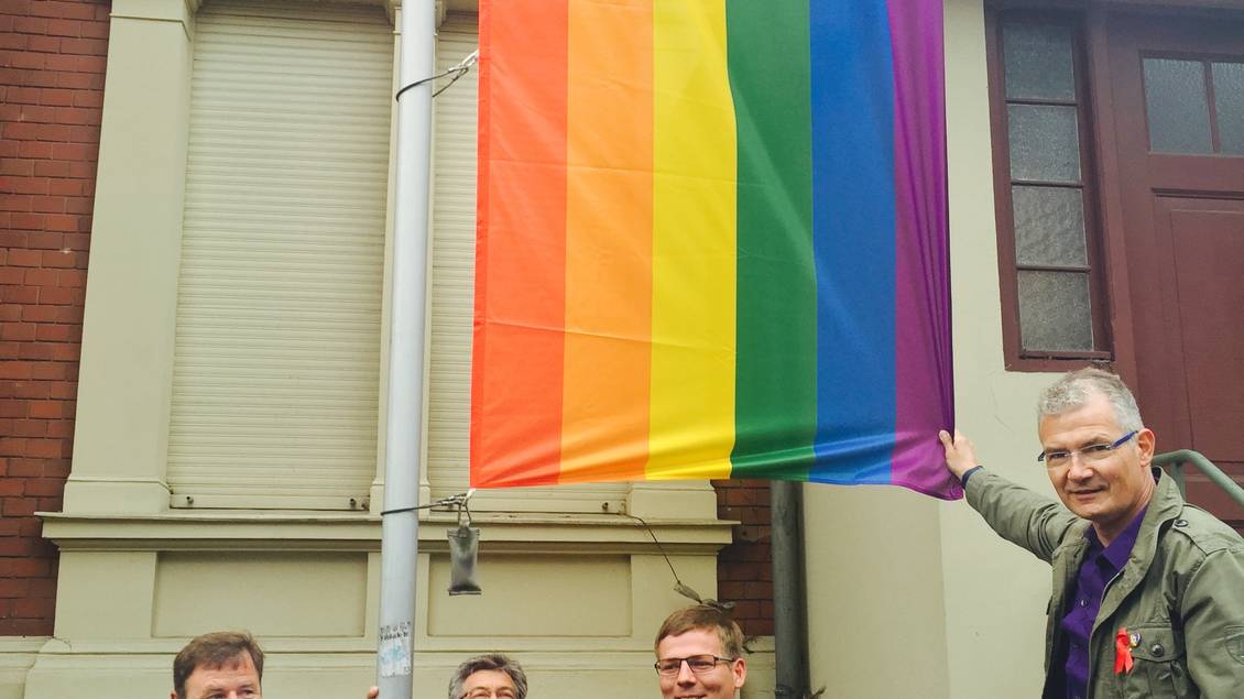 Christian Görke, Reinhard Frank, Sebastian Walter und Harald Petzold stehen an einem Fahnenmast, an dem eine Regenbogenfahne mit dem LINKE-Logo hängt