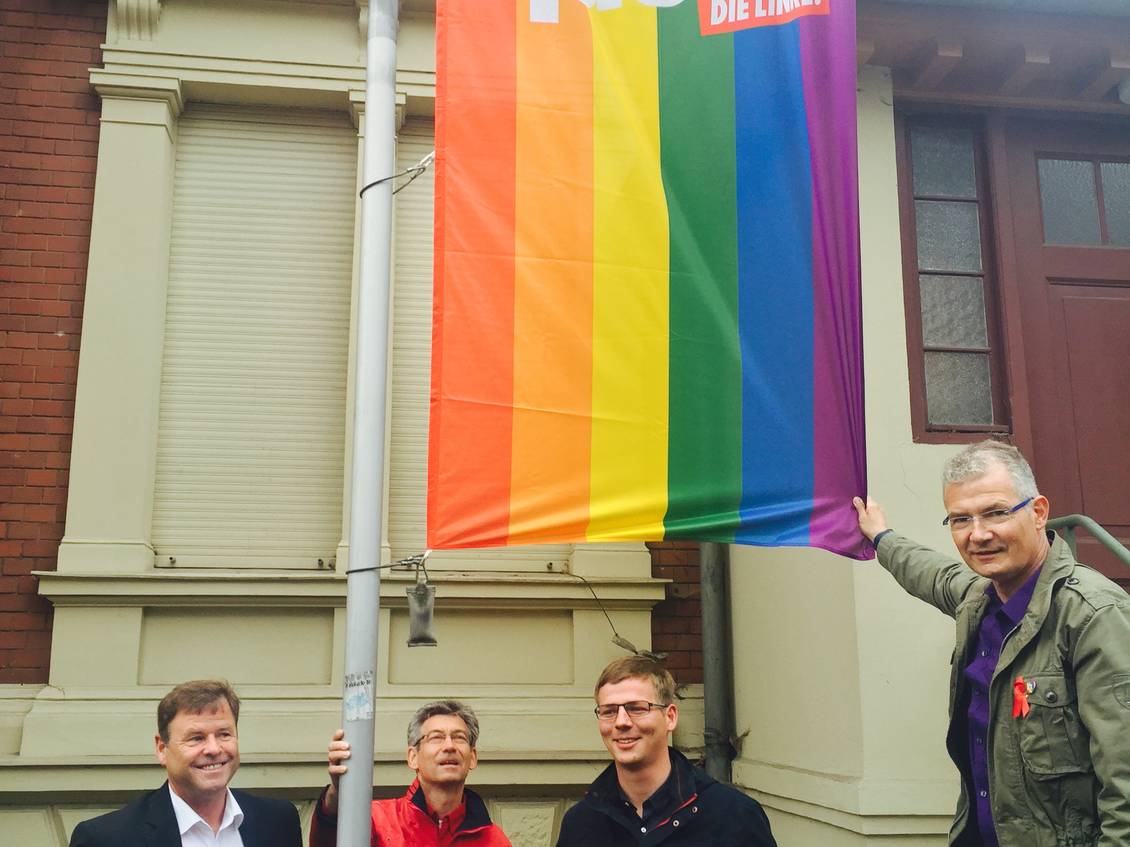 Christian Görke, Reinhard Frank, Sebastian Walter und Harald Petzold stehen an einem Fahnenmast, an dem eine Regenbogenfahne mit dem LINKE-Logo hängt