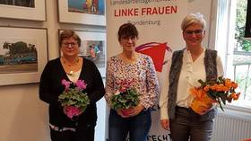 Ute Miething, Gabriele Brandt und Diana Bader stehen mit Blumensträußen in den Händen vor einem Roll-Up mit der Aufschrift "Landesarbeitsgemeinschaft LINKE Frauen Brandenburg"