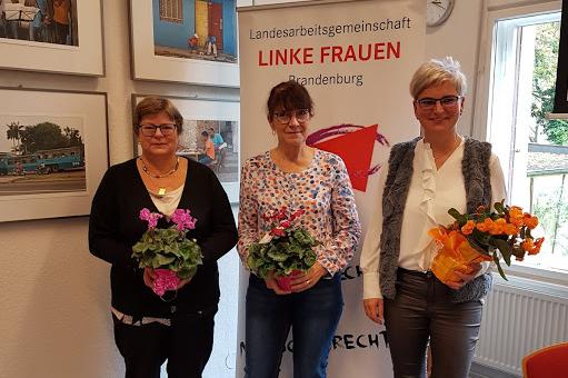 Ute Miething, Gabriele Brandt und Diana Bader stehen mit Blumensträußen in den Händen vor einem Roll-Up mit der Aufschrift "Landesarbeitsgemeinschaft LINKE Frauen Brandenburg"