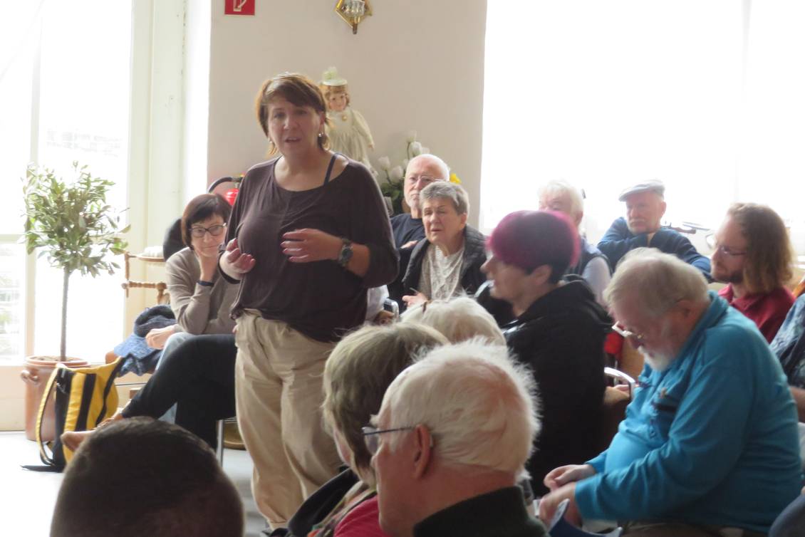 Katharina Slanina steht in einem Halbkreis aus Stühlen, auf denen die Teilnehmer sitzen