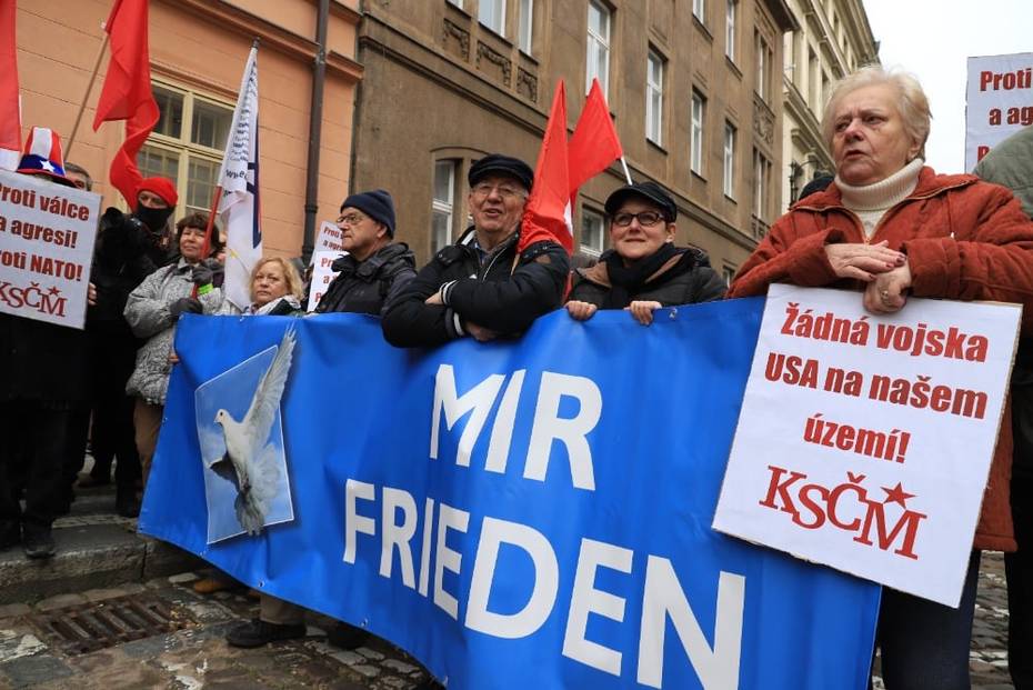 Teilnehmer der Kundgebung mit Schildern und roten Fahnen, mehrere Personen halten ein Transparent, auf das eine Friedenstaube sowie der Schriftzug "Mir - Frieden" gedruckt ist