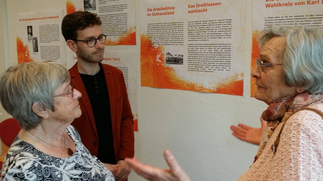 Tobias Bank und zwei ältere Damen stehen vor Ausstellungstafeln