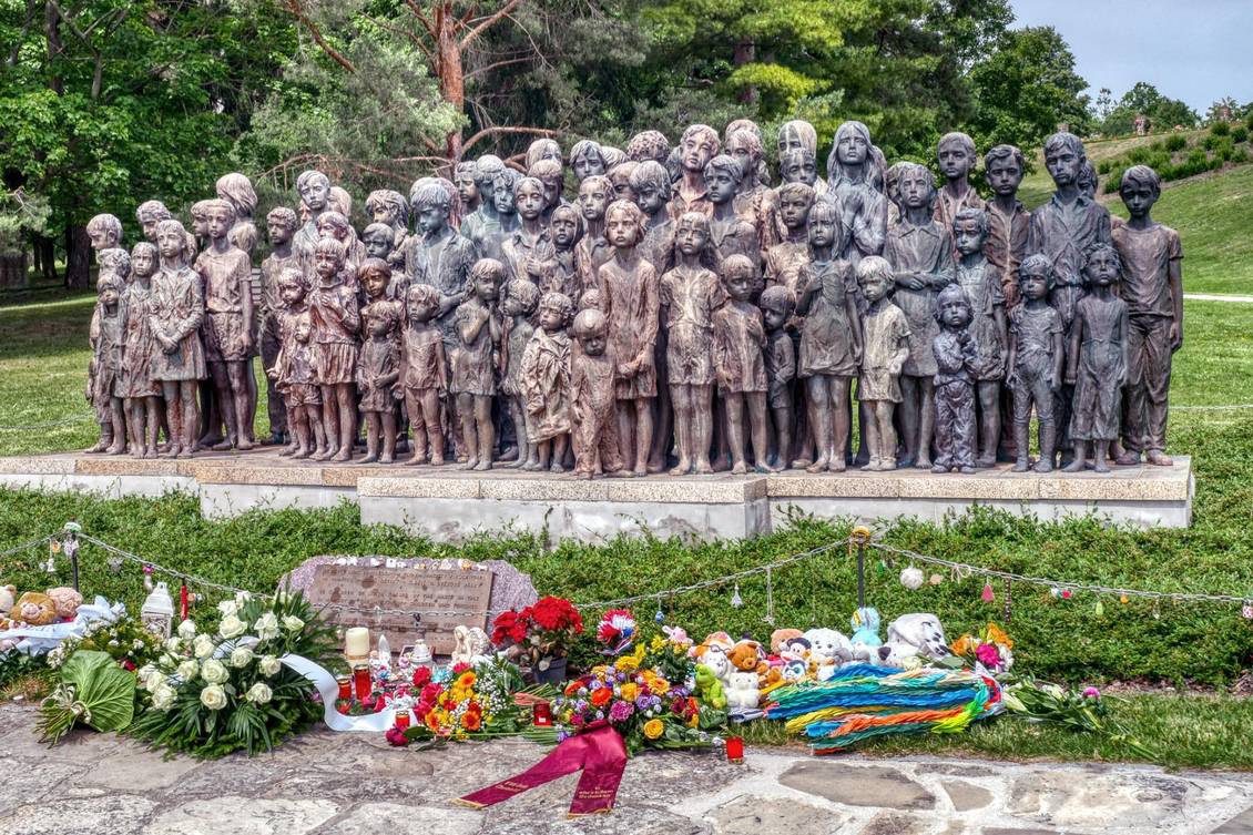 Eine Gruppe Bronzestatuen von Kindern, vor denen Blumen und Grablichter stehen