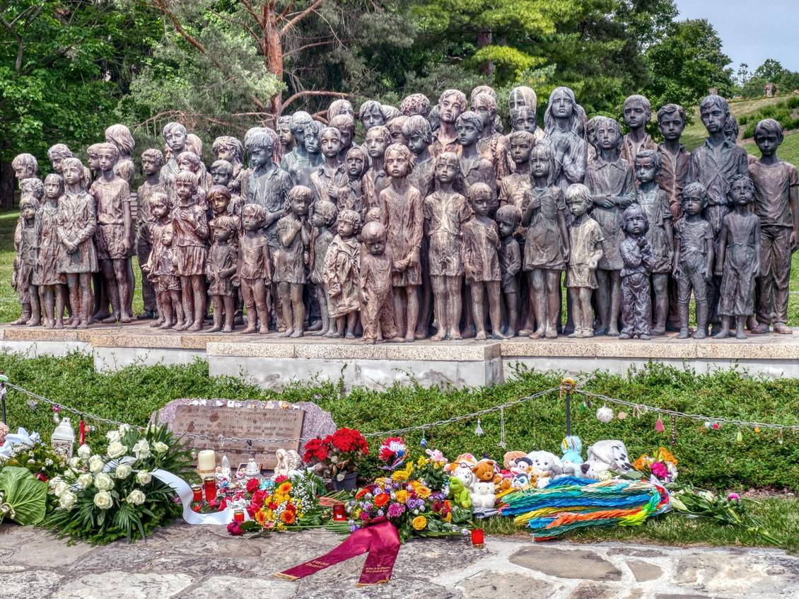 Eine Gruppe Bronzestatuen von Kindern, vor denen Blumen und Grablichter stehen