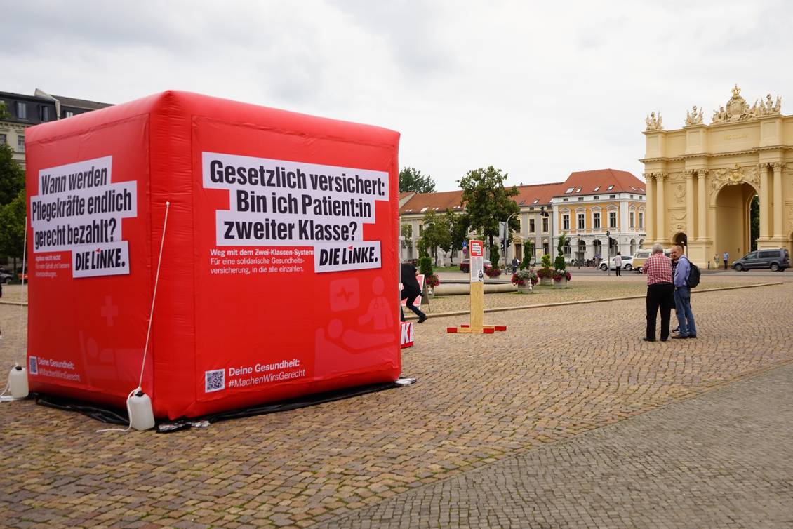 Luisenplatz in Potsdam, auf dem Platz steht ein 3x3 Meter großer aufblasbarer roter Würfel mit dem Logo der LINKEN und verschiedenen Aussagen zu den Themen Pflege und Gesundheit