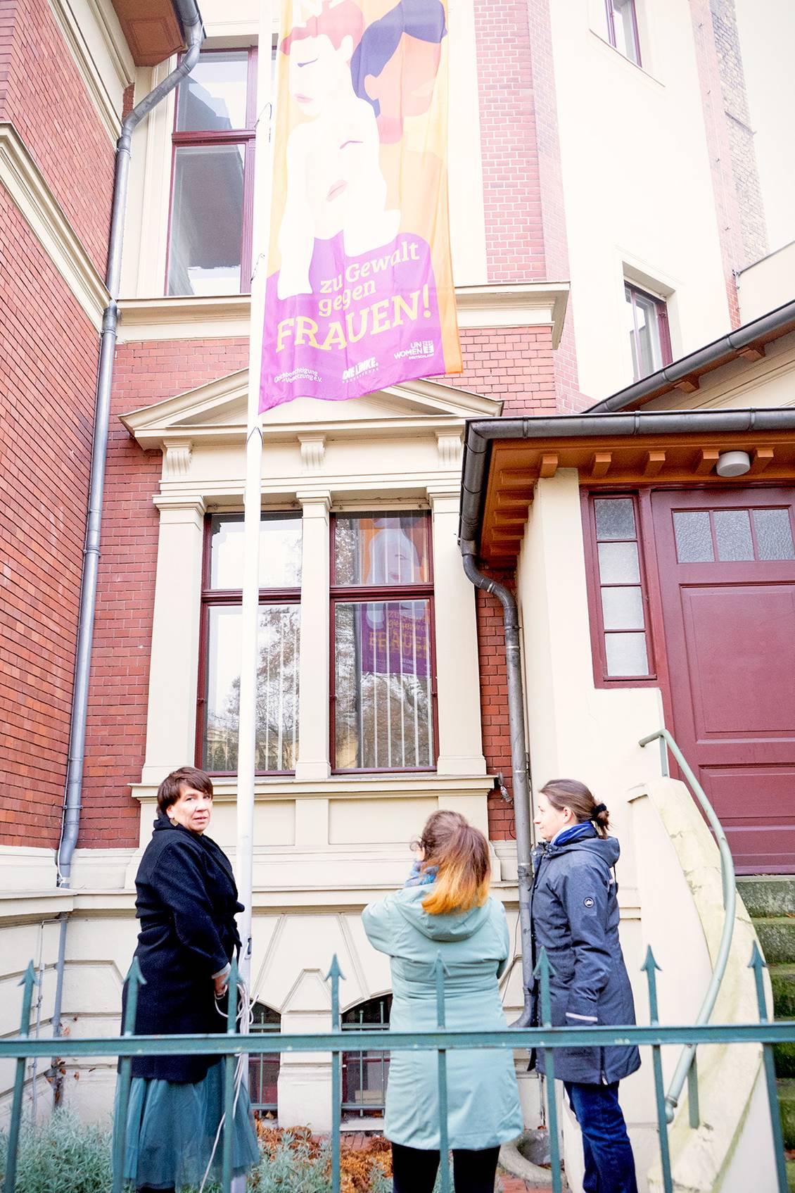 Katharina Slanina, Claudia Sprengel und Julia Wiedemann hissen die UN-Women-Flagge an einem Fahnenmast vor dem Lothar-Bisky-Haus