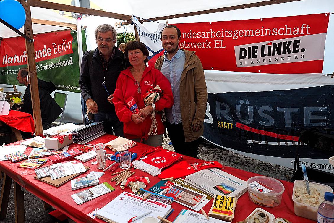 Jaroslav Růžička und zwei weitere Personen stehen an einem Infostand, auf dem Zeitungen liegen