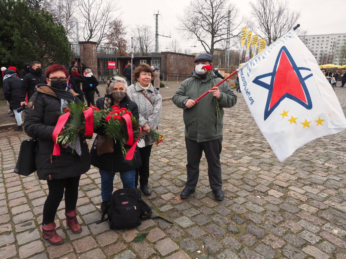 Gruppenbild der LAG Netzwerk EL vor dem Friedhof der Sozialisten in Berlin-Friedrichsfelde, eine Person hält eine Fahne mit dem Logo der Europäischen Linken
