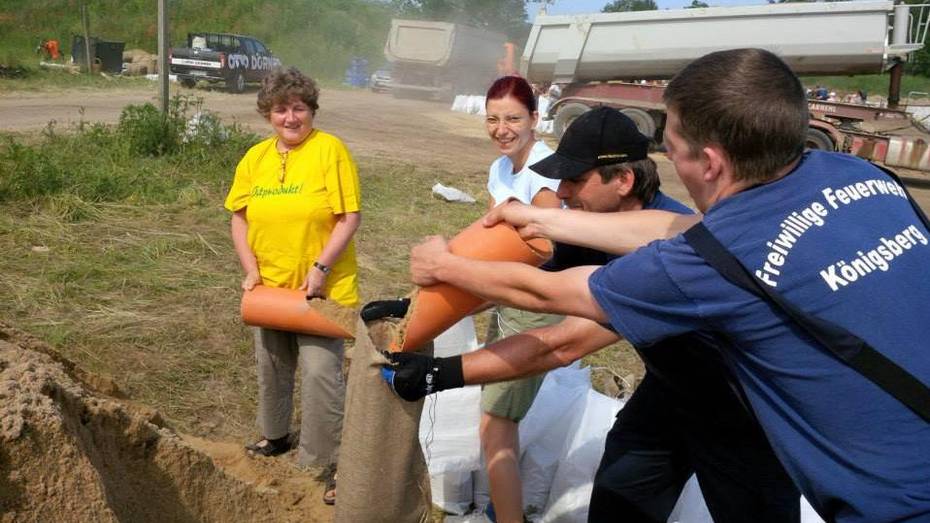 Kirsten Tackmann, Diana Golze und zwei Herren mit T-Shirts der Freiweilligen Feuerwehr Königsberg füllen Sand in Sandsäcke