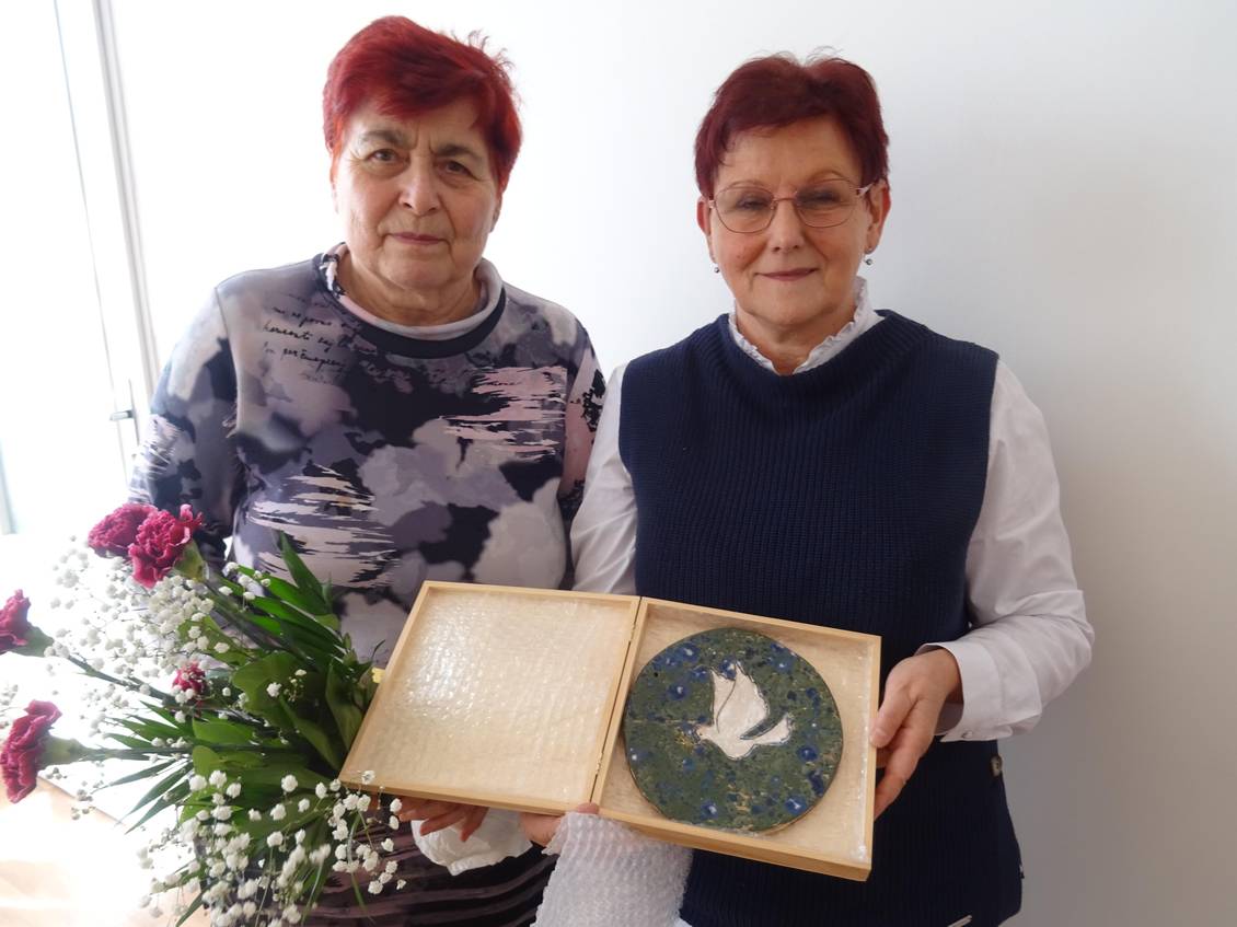Alena Grospičová und Monika Schömmel stehen nebeinander und halten gemeinsam einen Keramikteller mit einer Friedenstaube in die Kamera