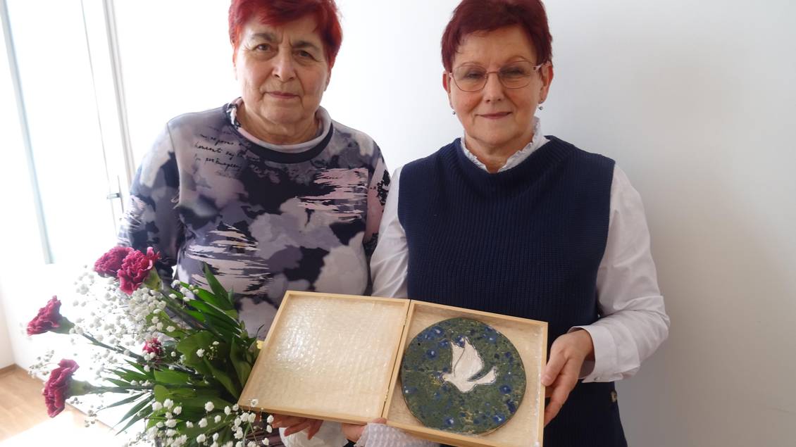 Alena Grospičová und Monika Schömmel stehen nebeinander und halten gemeinsam einen Keramikteller mit einer Friedenstaube in die Kamera