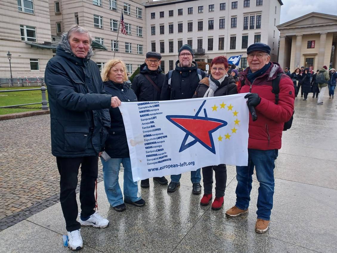 Mehrere Menschen stehen vor der US-Botschaft in Berlin und halten eine Fahne mit dem Logo der Europäischen Linken in den Händen