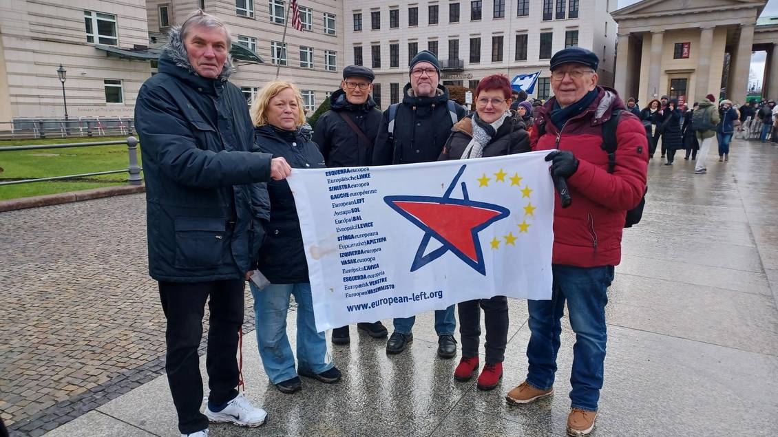 Mehrere Menschen stehen vor der US-Botschaft in Berlin und halten eine Fahne mit dem Logo der Europäischen Linken in den Händen