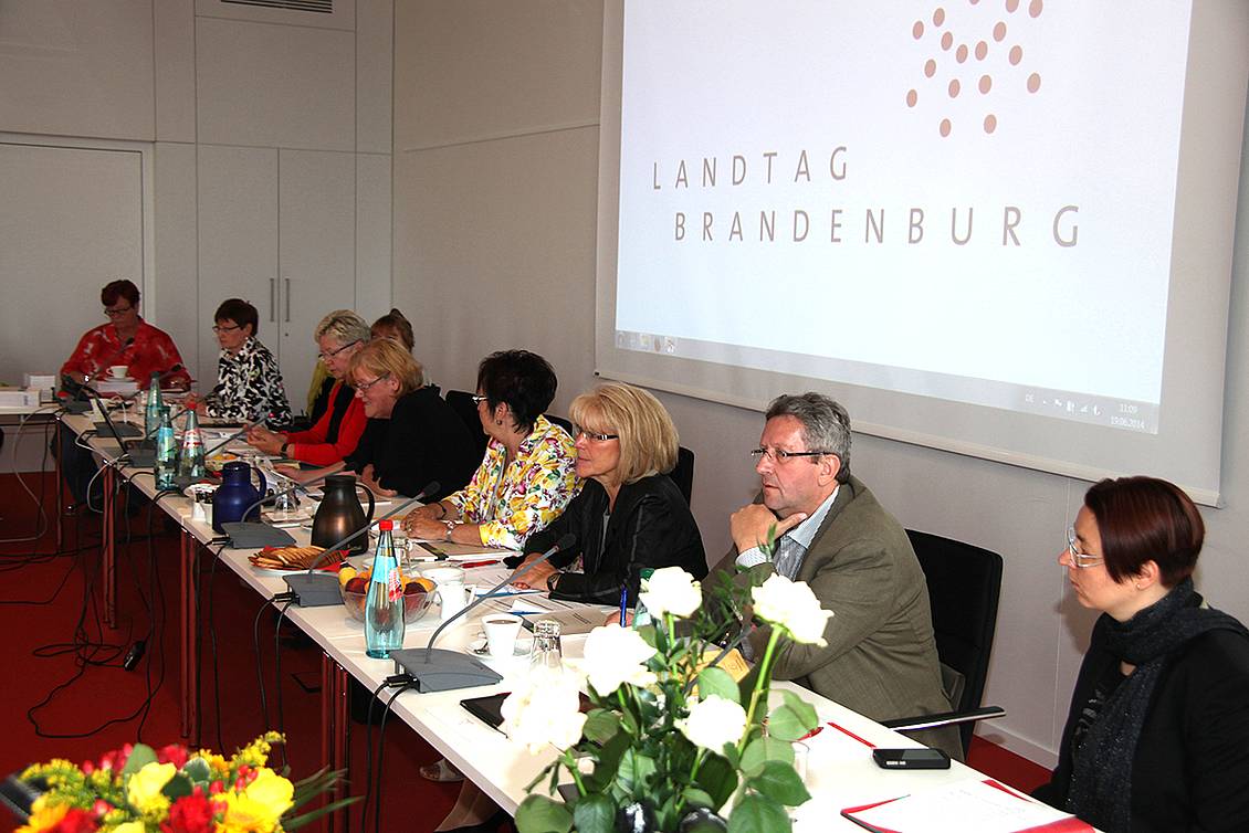 Konferenz in einem Besprechunsgraum mit Getränken auf den Tischen, an einem Tisch sitzt Kornelia Wehlan, an der Wand eine Powerpont-Folie auf der "Landtag Brandenburg" steht