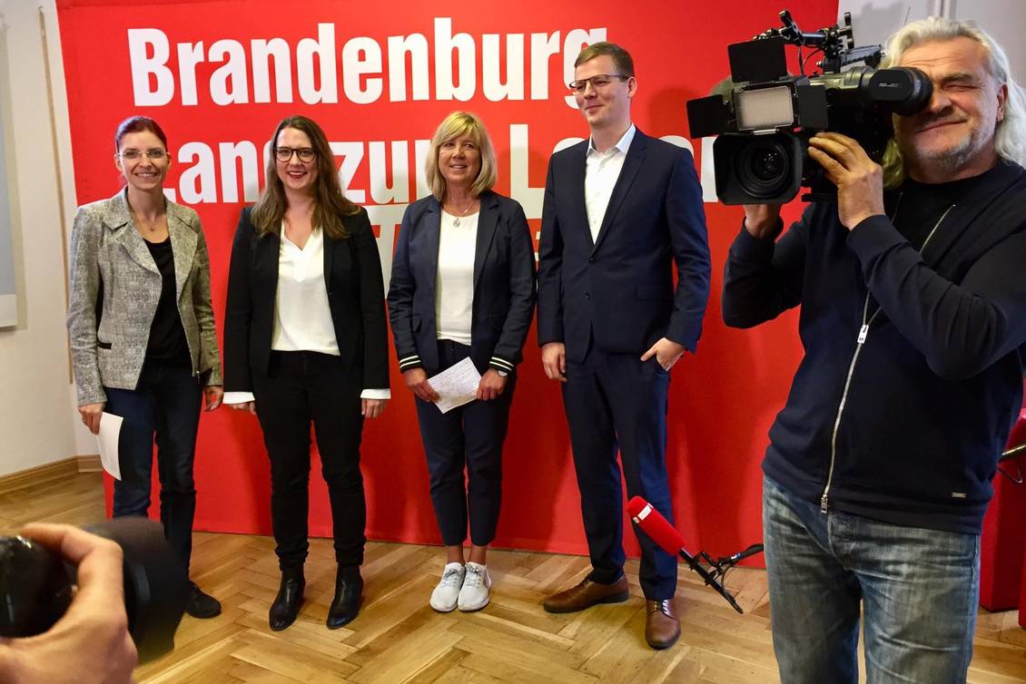 Diana Golze, Anja Mayer, Kathrin Dannenberg und Sebastian Walter stehen vor einer Präsentationswand mit der Aufschrift: Brandenburg, Land zum Leben