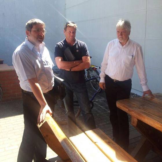Stefan Ludwig, Christian Görke und Halmuth Markov stehen an einem Holztisch im Freien
