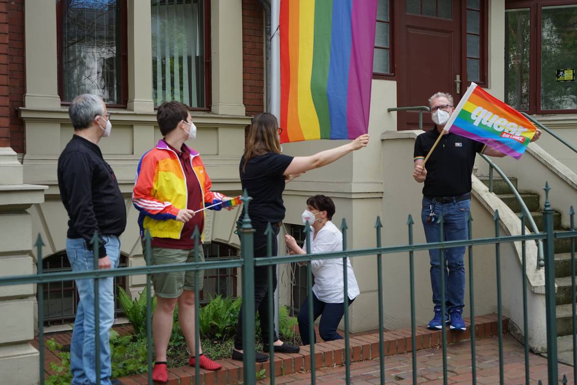 Anja Mayer und Katharina Slanina ziehen an einem Fahnenmast eine Regenbogen-Flagge in die Höhe, neben ihnen stehen Stefan Wollenberg, Anton und Carsten Schneider
