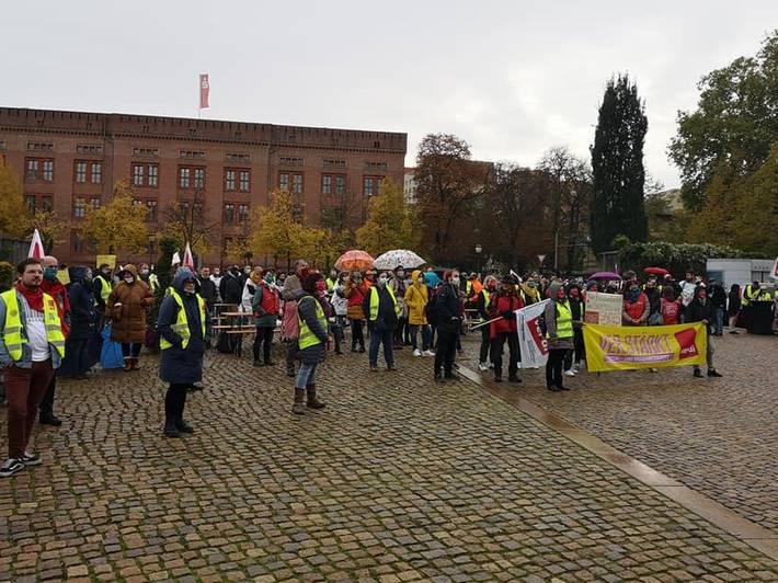Menschen mit Warnwesten und Transparenten stehen auf einem Platz mit Kopfsteinpflaster