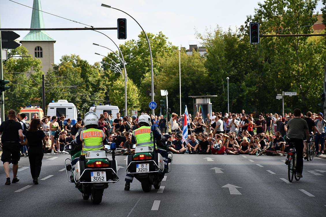 Demonstranten sitzen auf der Straße, davor zwei Polizisten mit Motorrädern
