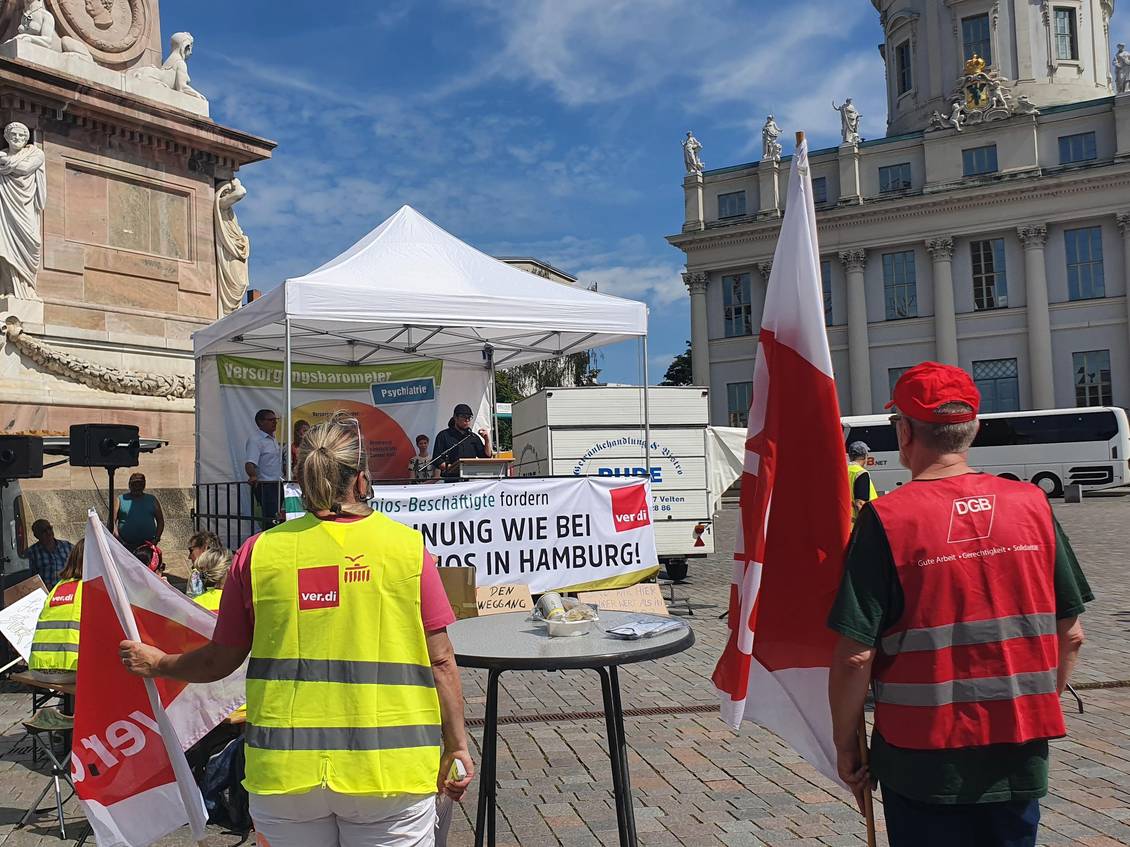 Menschen mit Warnwesten und Fahnen mit Logos der Gewerkschaften stehen vor dem Potsdamer Landtag, Norbert Müller steht unter einem Faltpavillon und spricht in ein Mikrofon