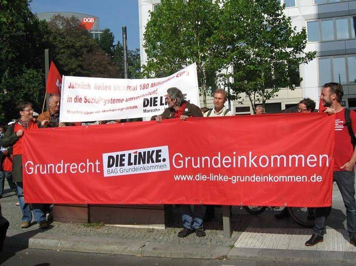 Demonstrierende mit Transparent, auf dem "Grundrecht Grundeinkommen - DIE LINKE. BAG Grundeinkommen" steht