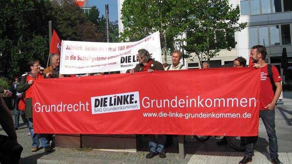 Demonstrierende mit Transparent, auf dem "Grundrecht Grundeinkommen - DIE LINKE. BAG Grundeinkommen" steht