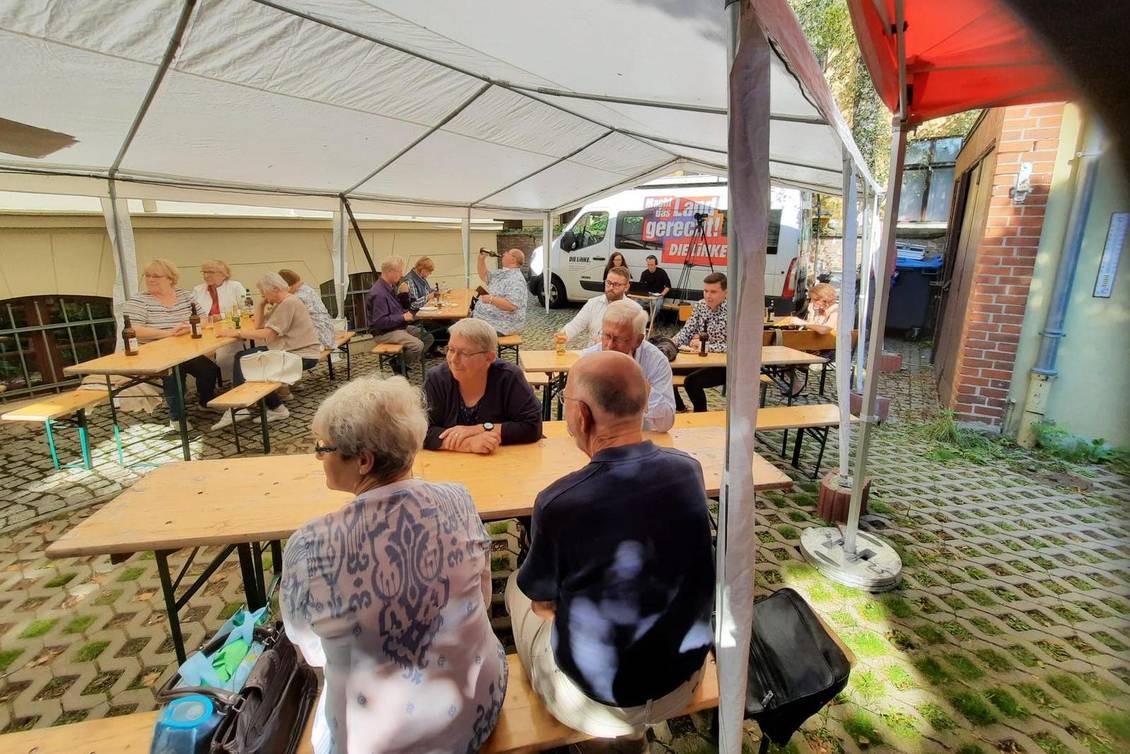 Mehrere Personen sitzen auf dem Hof des Lothar-Bisky-Hauses unter einem Festzelt auf Bierzeltgarnituren
