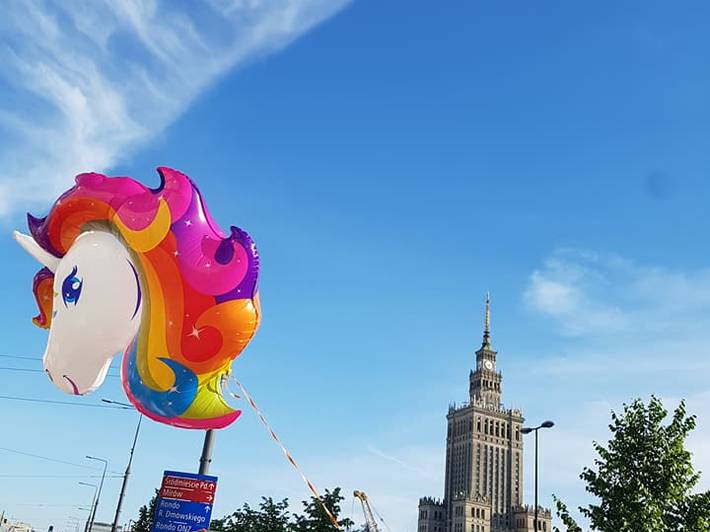 Menschen mit Regenbogen-Fahnen und einem Einhorn-Luftballon vor dem Kulturpalast in Warschau