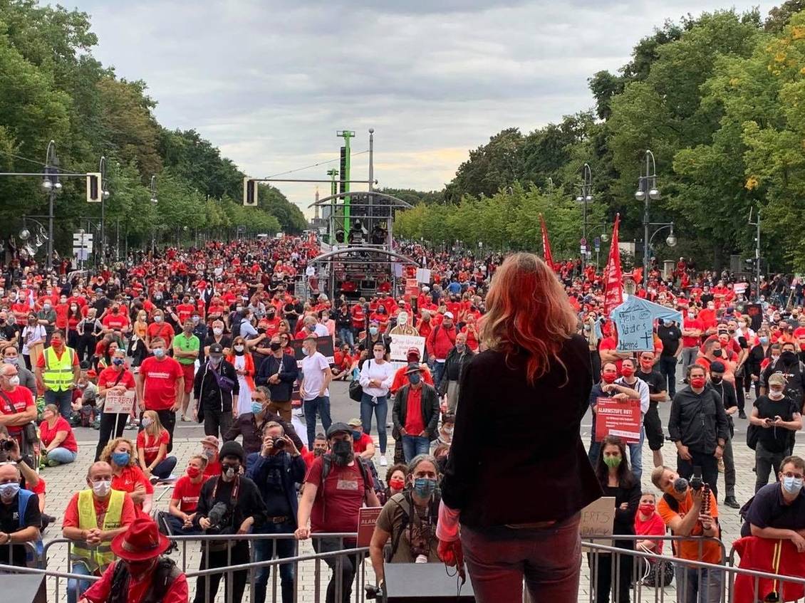 Caren Lay steht auf einer Bühne vor einer Menschenmenge, von denen viele ein rotes T-Short oder eine rote Weste tragen
