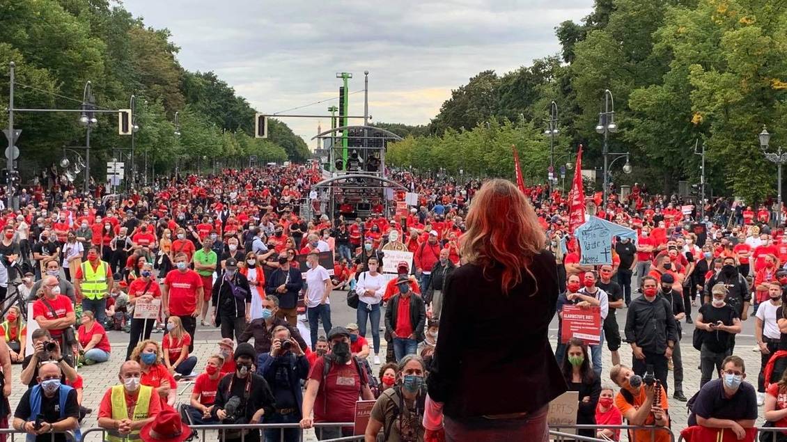 Caren Lay steht auf einer Bühne vor einer Menschenmenge, von denen viele ein rotes T-Short oder eine rote Weste tragen