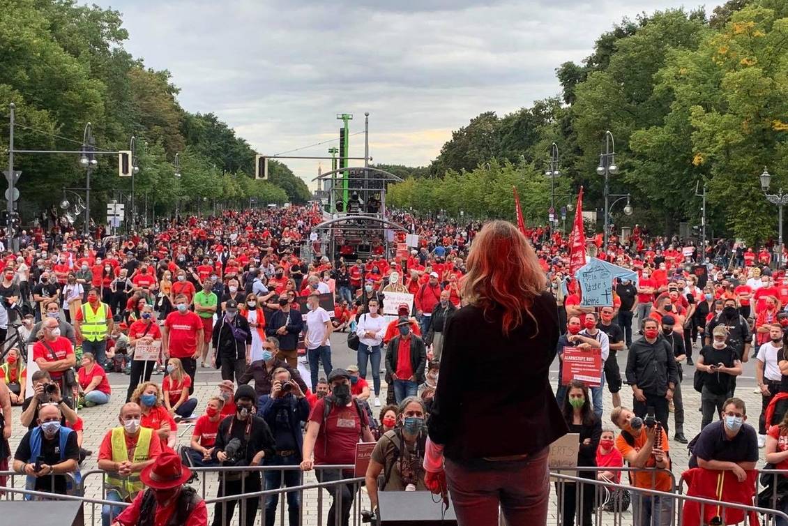 Caren Lay steht auf einer Bühne vor einer Menschenmenge, von denen viele ein rotes T-Short oder eine rote Weste tragen