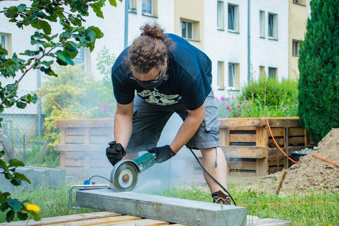 Ein Mann zerschneidet einen Randstein mit einem Winkelschleifer