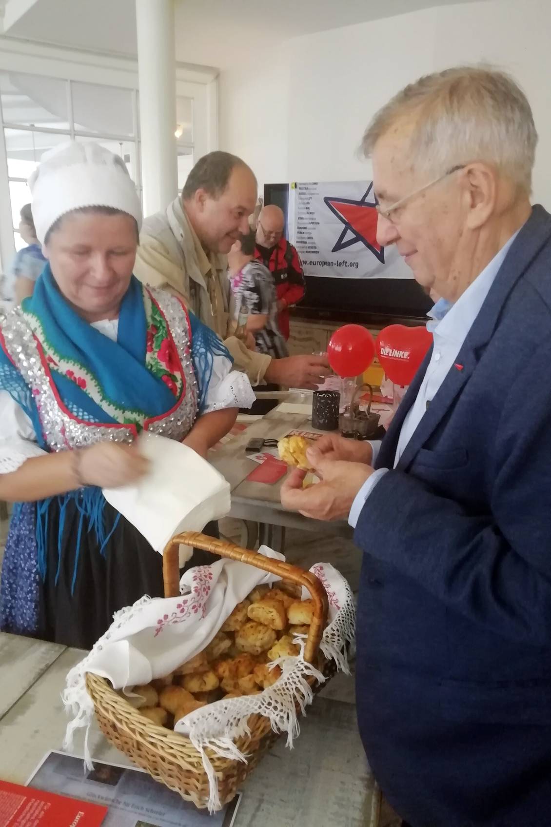 Eine in Tracht gekleidete Frau gibt einem Mann Gebäck aus einem Korb