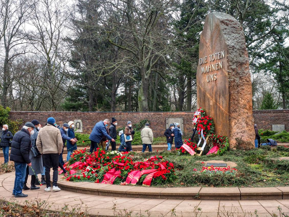 Gedenken am Gedenkstein mit der Aufschrift "Die Toten mahnen uns", mehrere Personen legen Blumen nieder