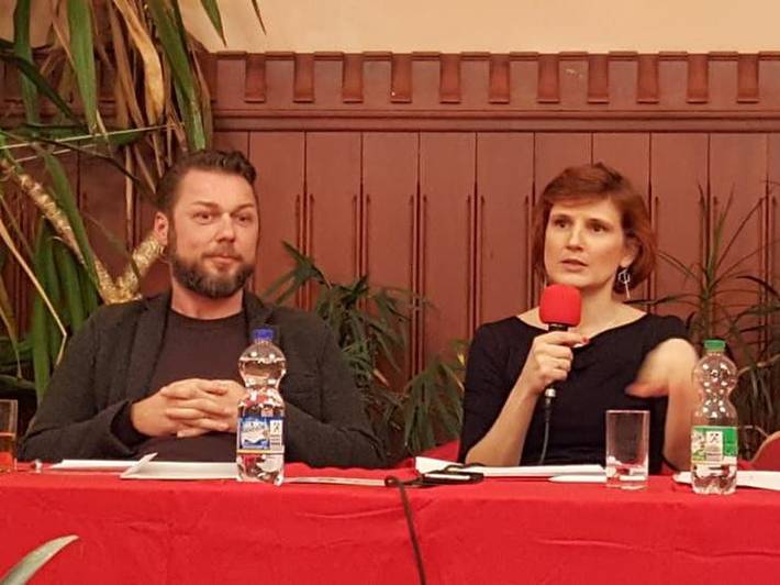 Ringo Jünigk und Katja Kipping mit Mikrofon in der Hand sitzen an einem Tisch mit roter Tischdecke