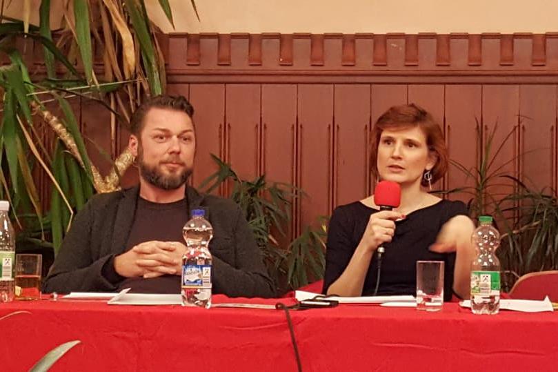 Ringo Jünigk und Katja Kipping mit Mikrofon in der Hand sitzen an einem Tisch mit roter Tischdecke